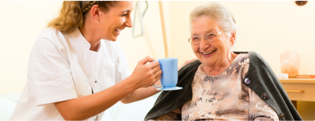 Carer sharing a warm cup of tea with an elderly lady at home